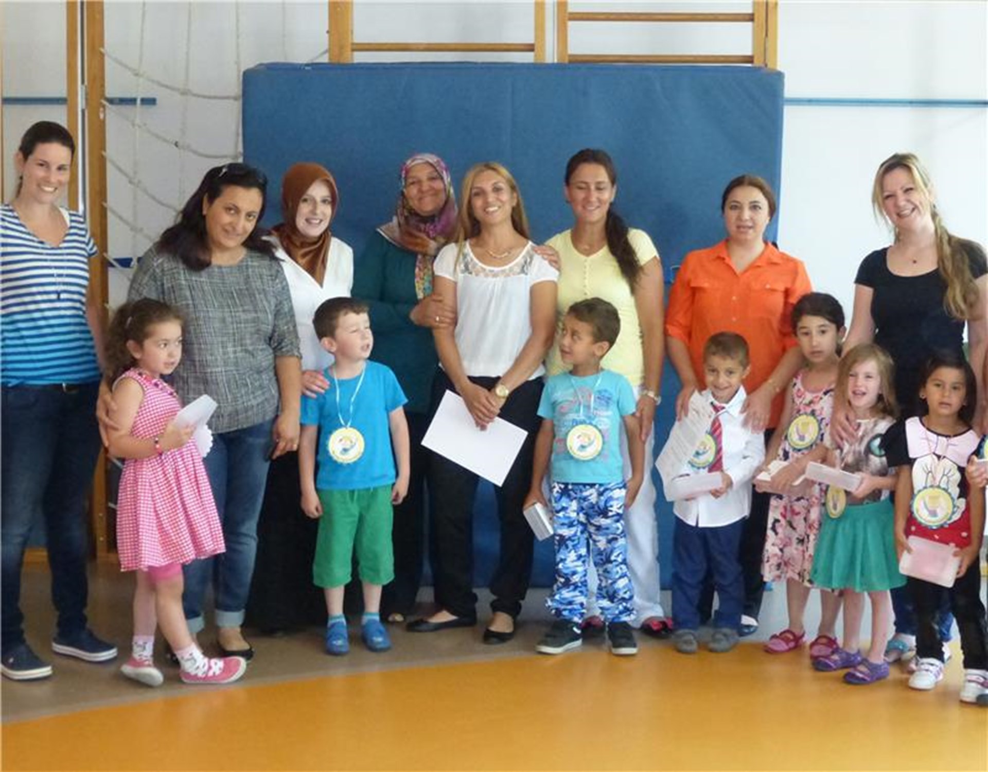ein Gruppe Eltern und Kinder stehen im Halbkreis in einer Turnhalle